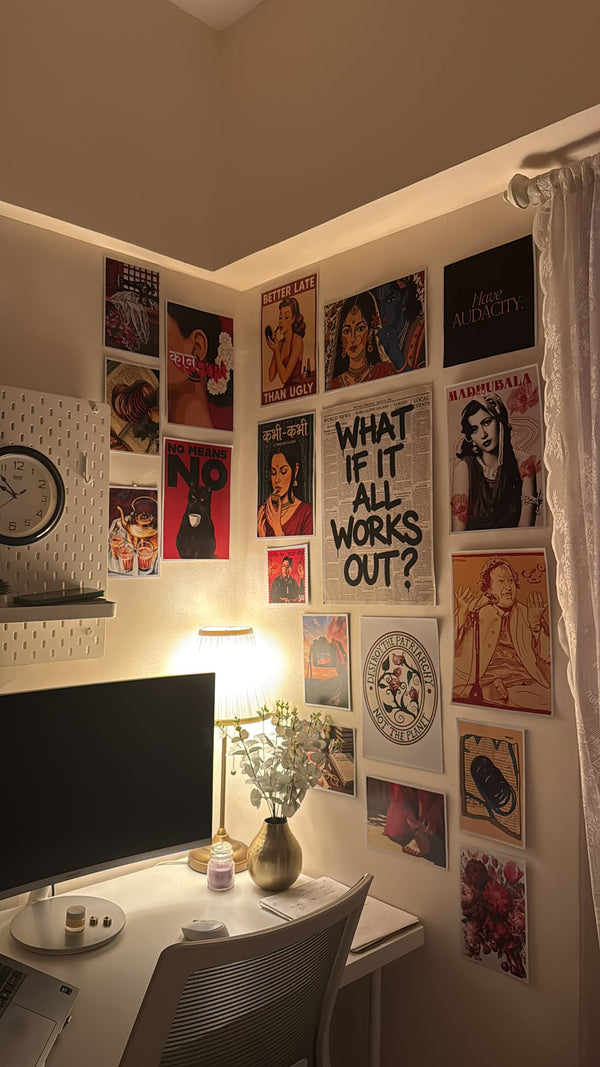 A cozy home office corner with a desk, computer monitor, lamp, and a wall covered in framed posters and art prints. The warm lighting casts a soft glow across the beige walls, and the room has a curtain on the right side. Posterwa